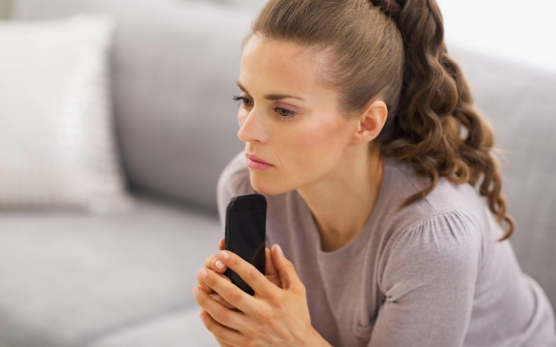 Mujer preocupada con un teléfono en las manos, reflexionando sobre qué pasa si no pago un préstamo en línea.